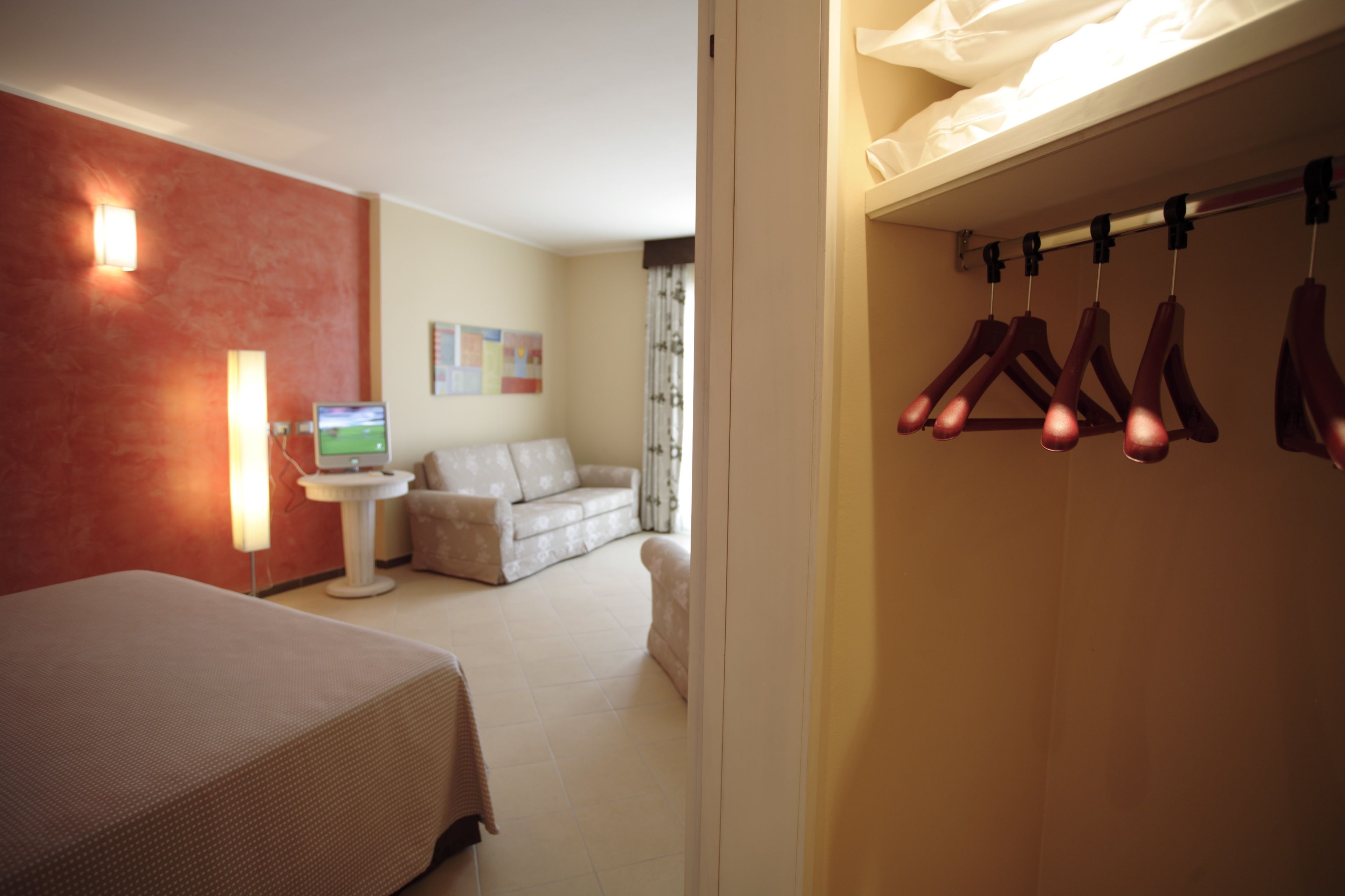 Una habitación de hotel con una cama, una pequeña mesa con lámpara, un sofá y un televisor.