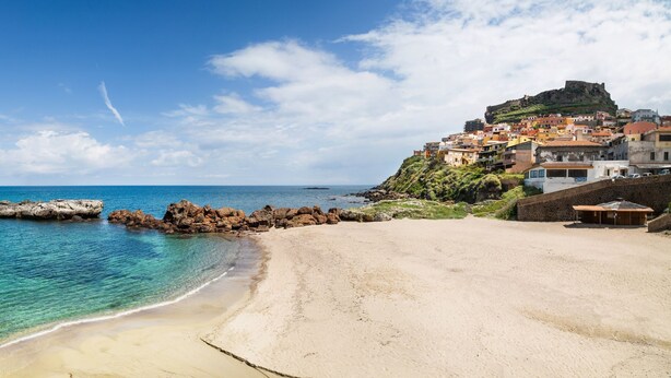 A coastal town with a beach, rocky shoreline, and a historic hilltop castle. - Janus Hotel (Castelsardo)