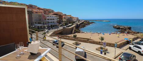 A balcony with a table and chairs, overlooking a beach with people and cars.