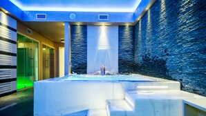 A spa area with a large hot tub, a waterfall feature, and a modern design with blue and white tones. - Janus Hotel (Castelsardo)