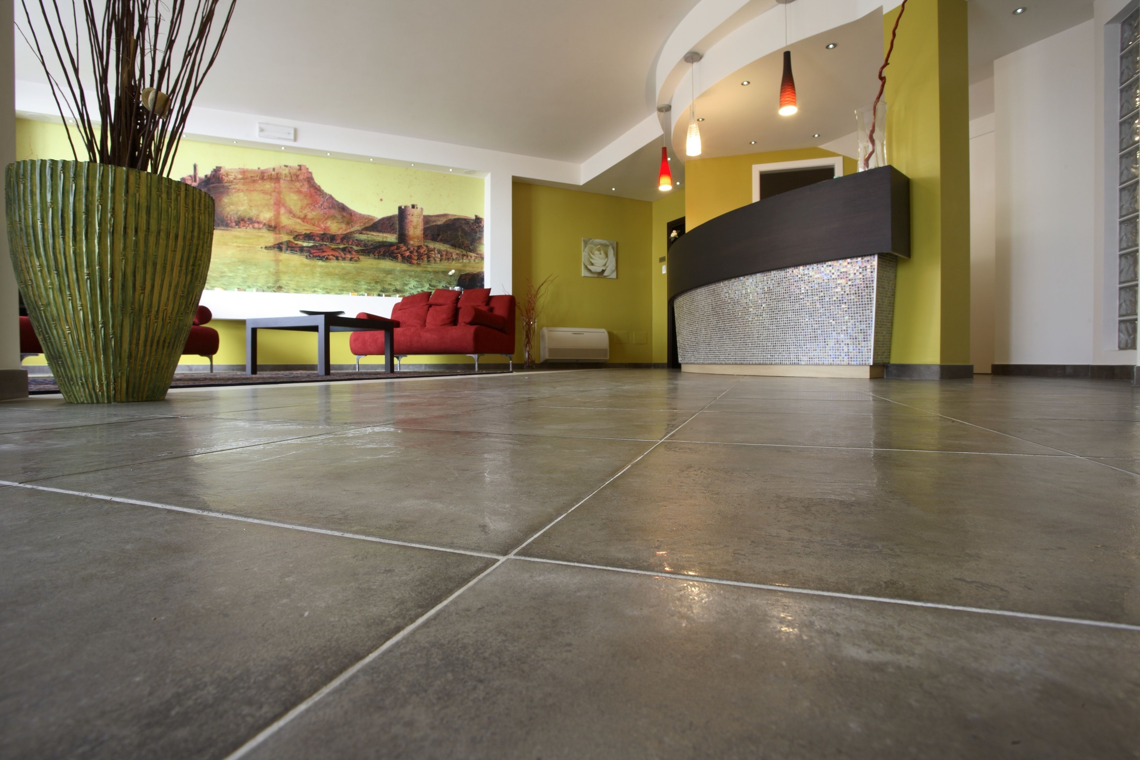 A lobby with a tiled floor, a red sofa, a large green vase, and a wall painting.