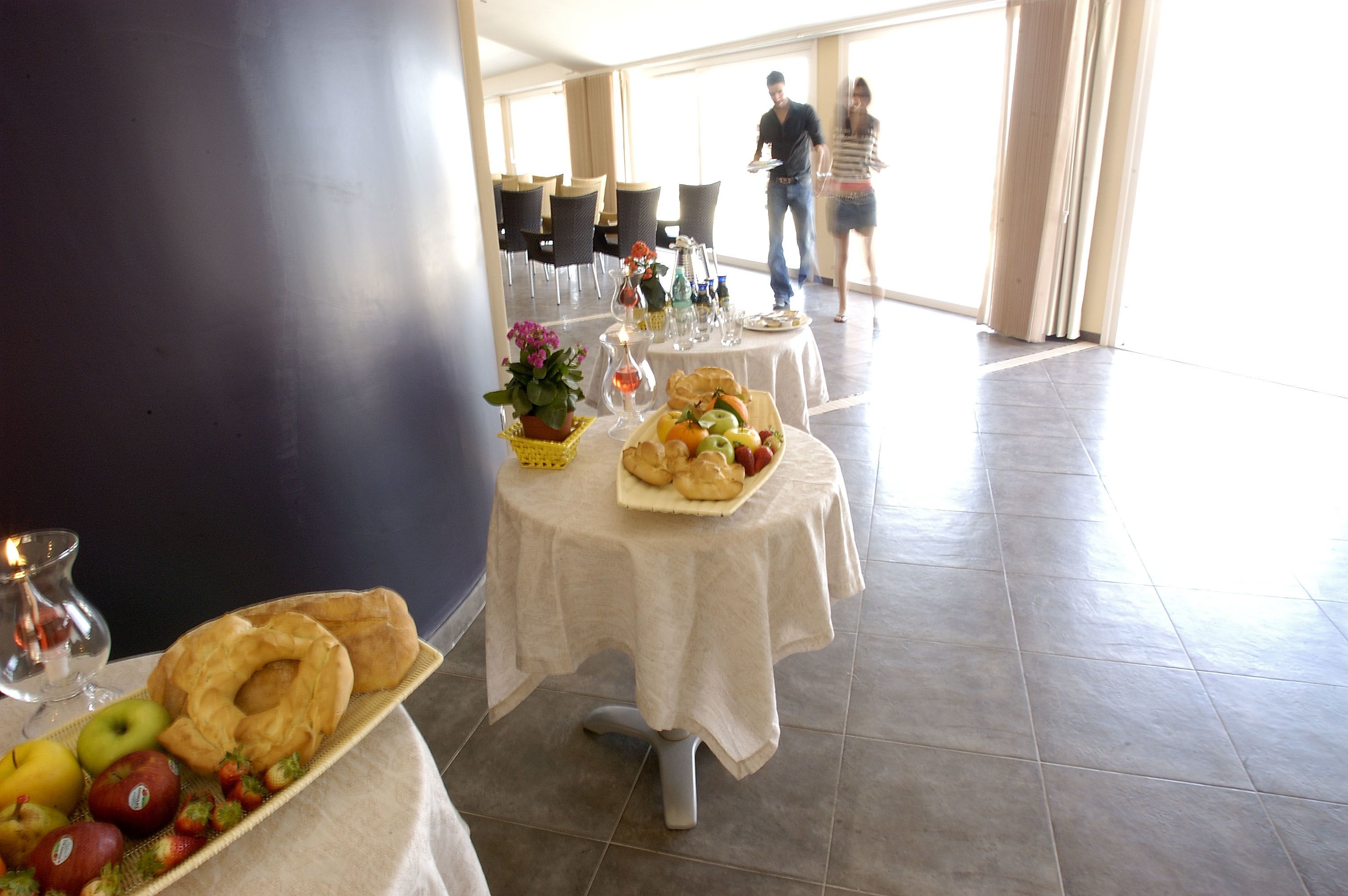 Comedor con mesas dispuestas para el desayuno, con frutas, pasteles y bebidas.