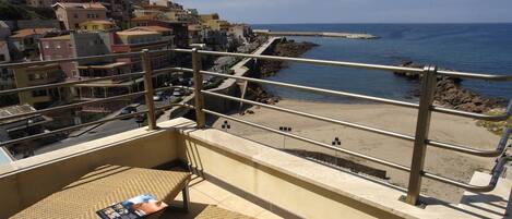A balcony with a view of a coastal town, a beach, and a rocky breakwater.