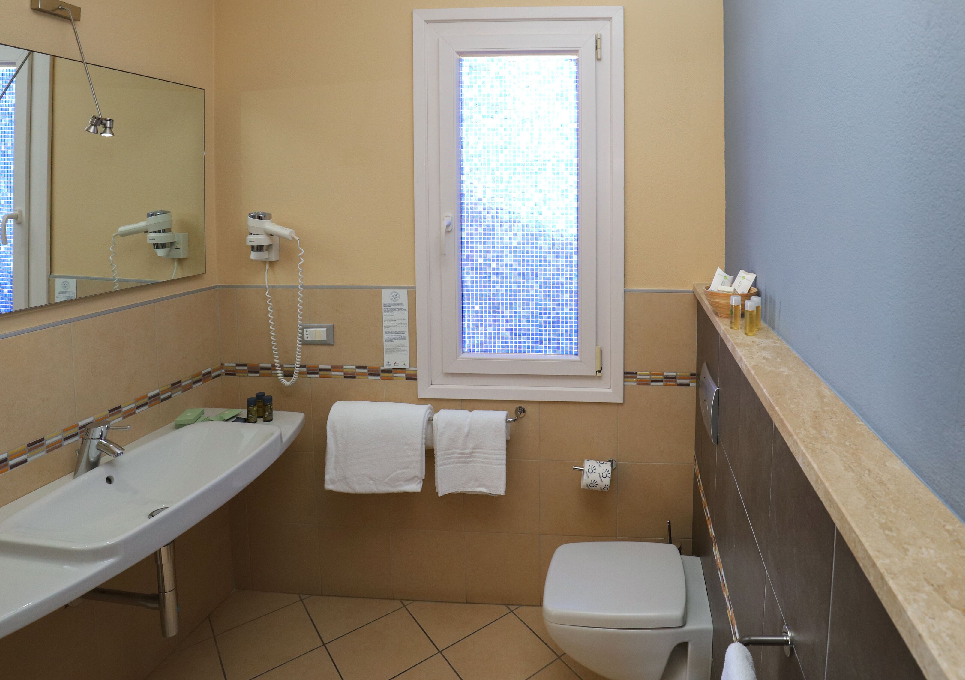 Un baño con lavamanos, inodoro, espejo y ventana con diseño de mosaico.