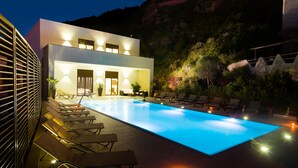 A modern pool area with lounge chairs, a pool, and a building with exterior lighting. - Janus Hotel (Castelsardo)