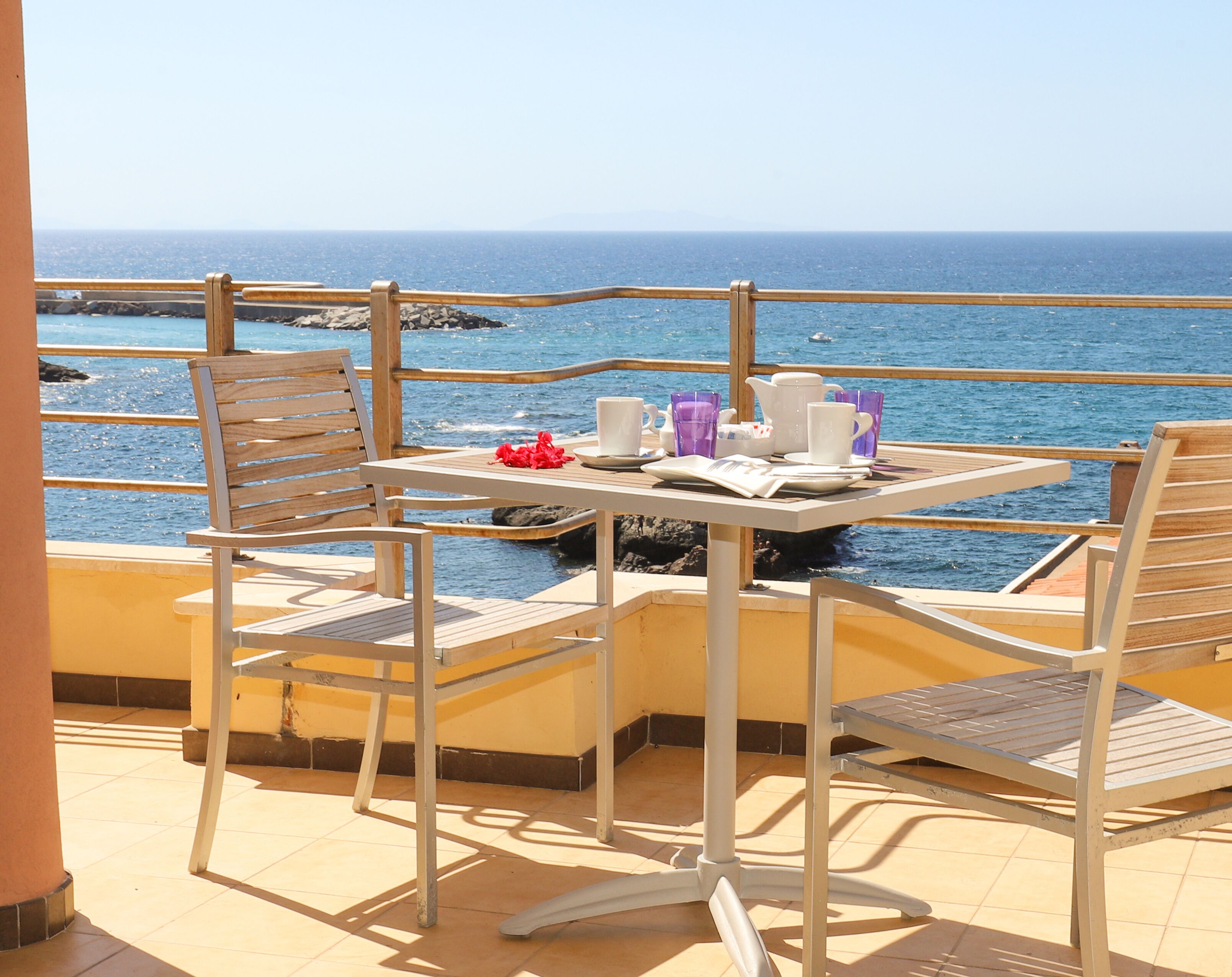 Eine Terrasse mit Tisch für Zwei mit Blick auf eine felsige Küste.