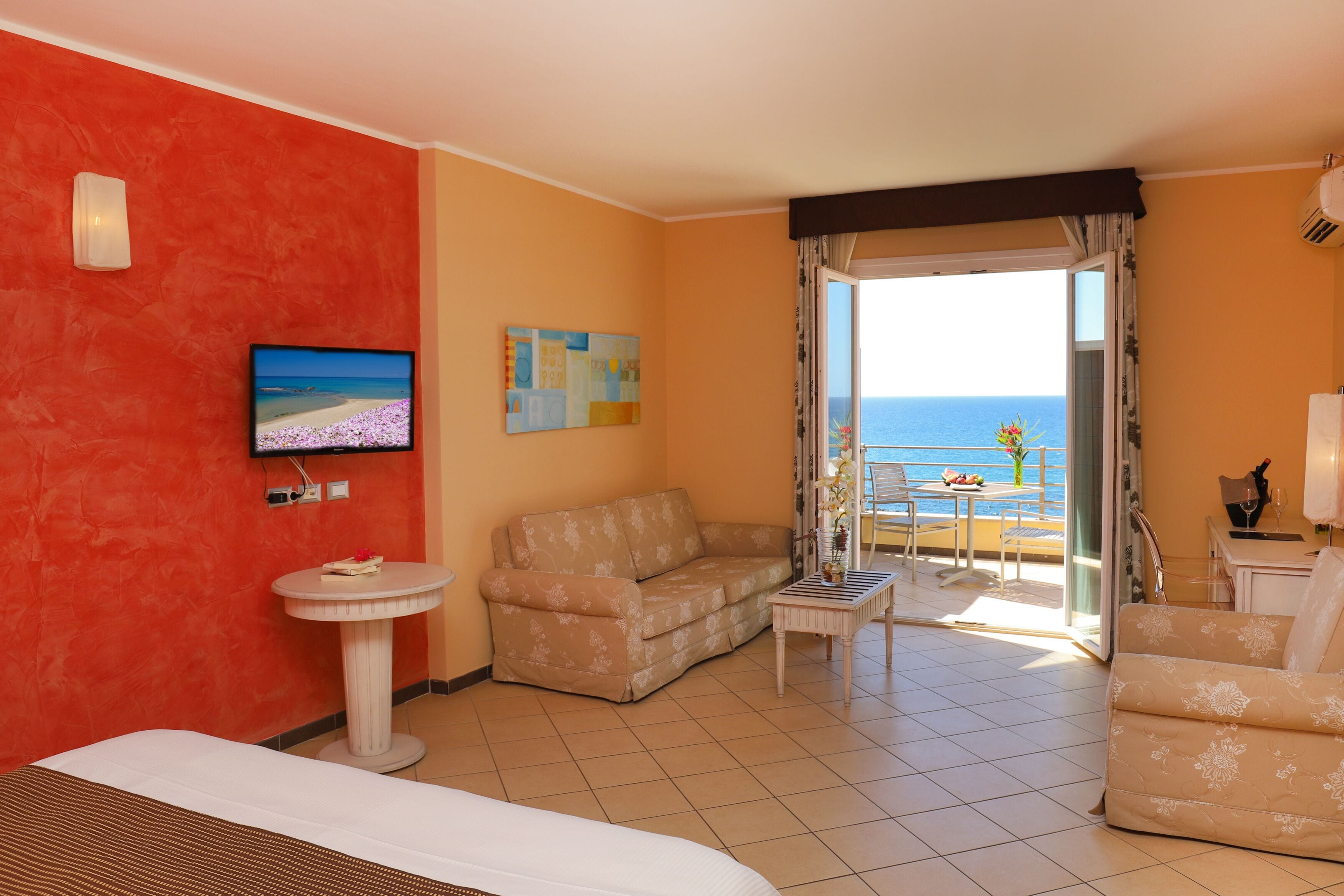 Une chambre d’hôtel comprenant un lit, un canapé, une petite table, une télévision et un balcon avec vue sur la mer.