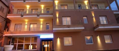 A multi-story hotel with balconies, a well-lit entrance, and a modern architectural design.