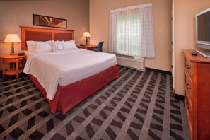 A hotel room with a large bed, two bedside tables with lamps, a television on a wooden cabinet, and a window with curtains.