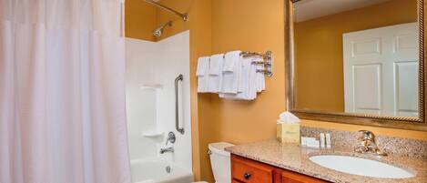 A bathroom with a bathtub, toilet, vanity with a sink, and a mirror.