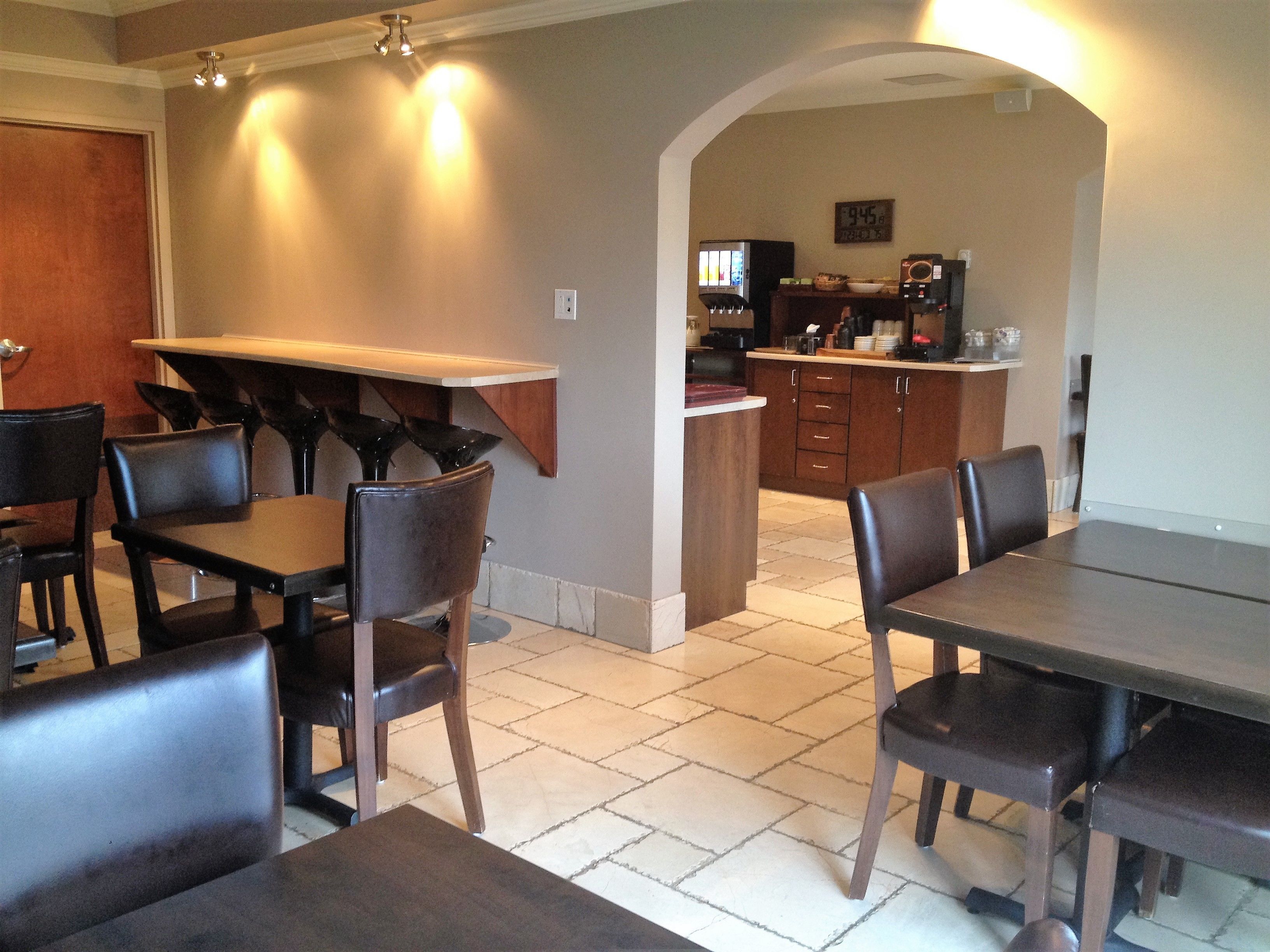 A dining area with a long table and chairs, a kitchen in the background, and a clock on the wall.