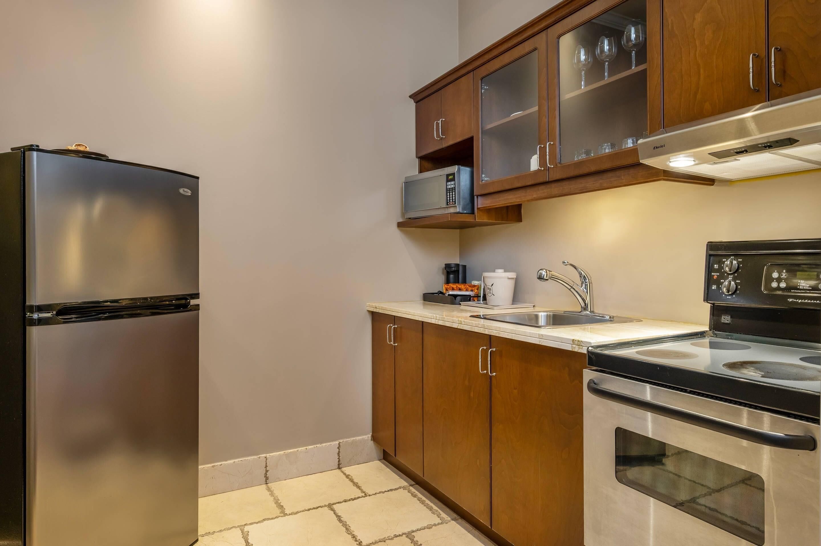 Una cocina compacta con refrigerador de acero inoxidable, microondas, estufa y armarios de madera.
