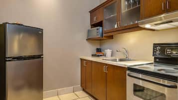 Una cocina compacta con refrigerador de acero inoxidable, microondas, estufa y armarios de madera.