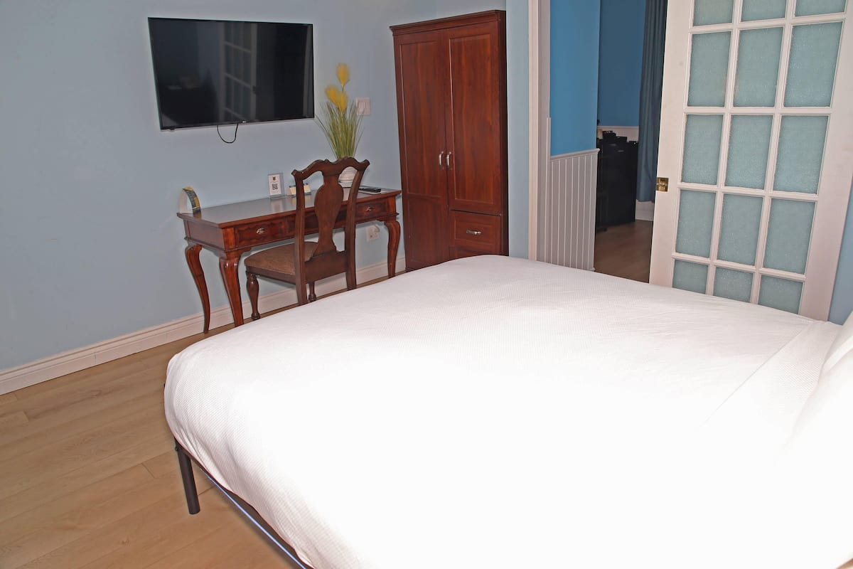 A bedroom with a bed, a desk, a chair, a wardrobe, and a television mounted on the wall.