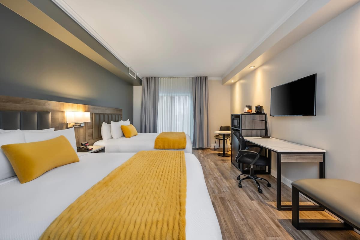 A hotel room with a bed, a desk, a chair, a TV, and a window with curtains.