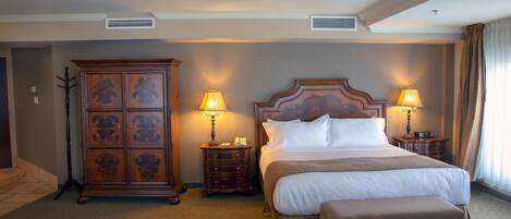 A hotel room with a large bed, two bedside tables with lamps, a wooden wardrobe, and a carpeted floor.