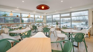 A modern dining area with tables and chairs, large windows, and a view of the parking lot. - Hotel Brossard, an Ascend Collection Hotel (Brossard)