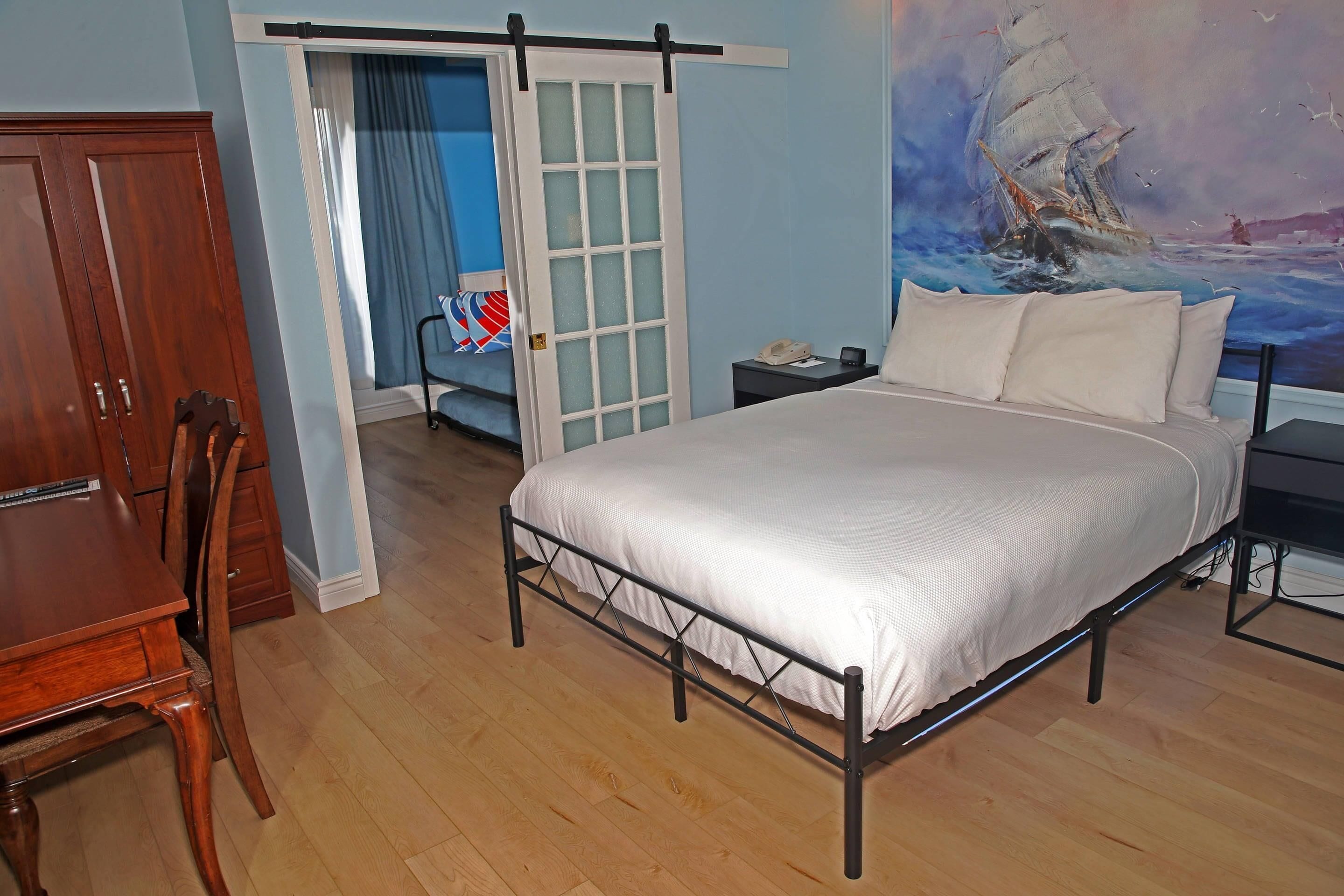 A bedroom with a bed, a wooden wardrobe, a desk, and a chair.