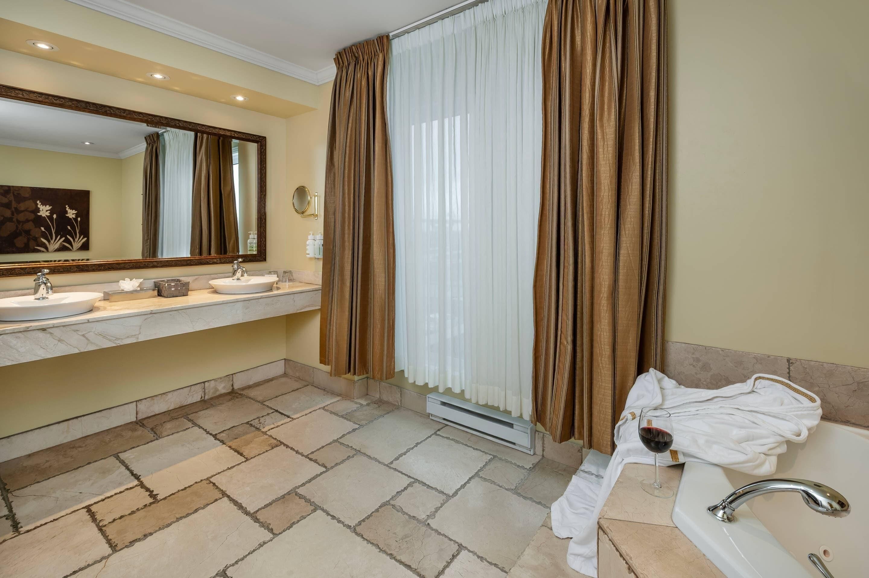 Un baño con dos lavamanos, un espejo, una ventana con cortinas y un perchero para toallas.