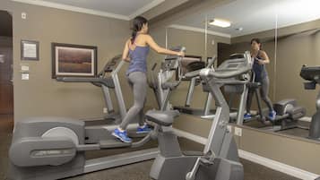 Un gimnasio con cintas de correr y equipamiento de ejercicio, un espejo y un cuadro en la pared.