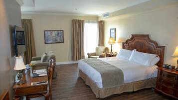 A hotel room with a large bed, a desk with a lamp, a chair, a television, and a painting on the wall.