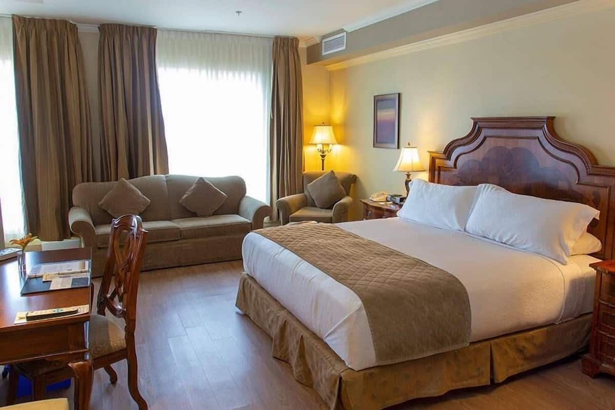 A hotel room with a bed, two armchairs, a desk, and a lamp.