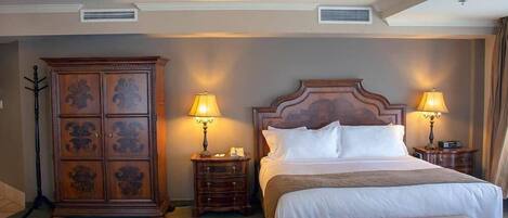 A hotel room with a large bed, two bedside tables with lamps, a wooden cabinet, and a ceiling vent.