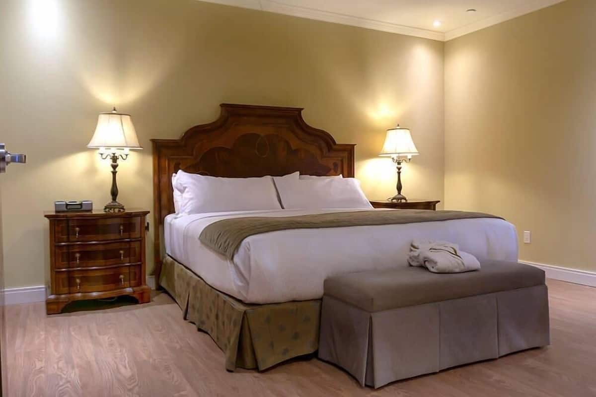 A hotel room with a large bed, two bedside lamps, a wooden nightstand, and a bench.