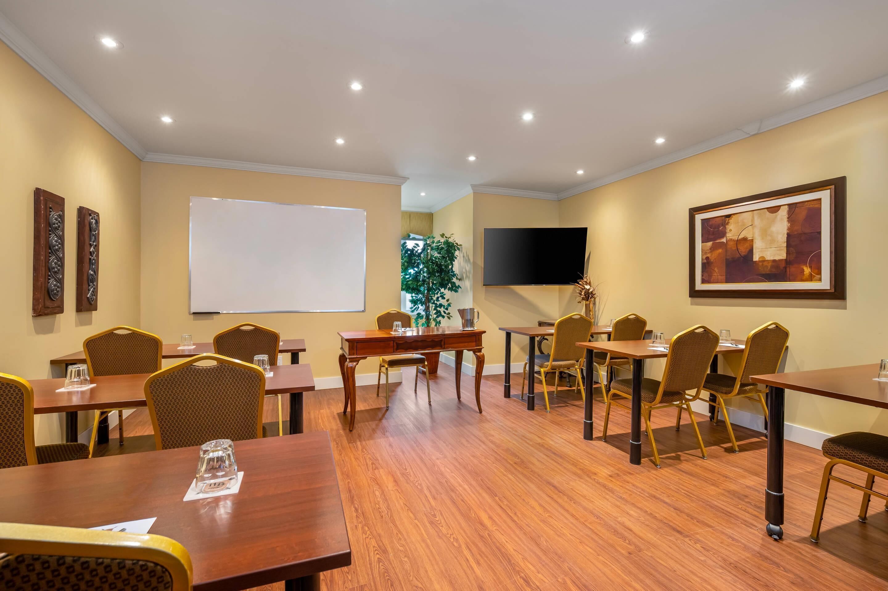 A conference room with wooden tables and chairs, a whiteboard, a flat-screen TV, and a painting on the wall.