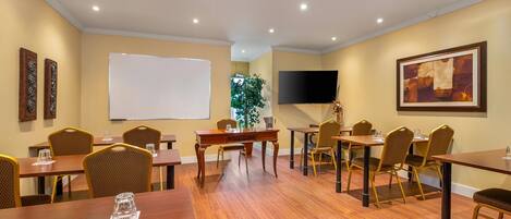 A conference room with wooden tables and chairs, a whiteboard, a flat-screen TV, and a painting on the wall.