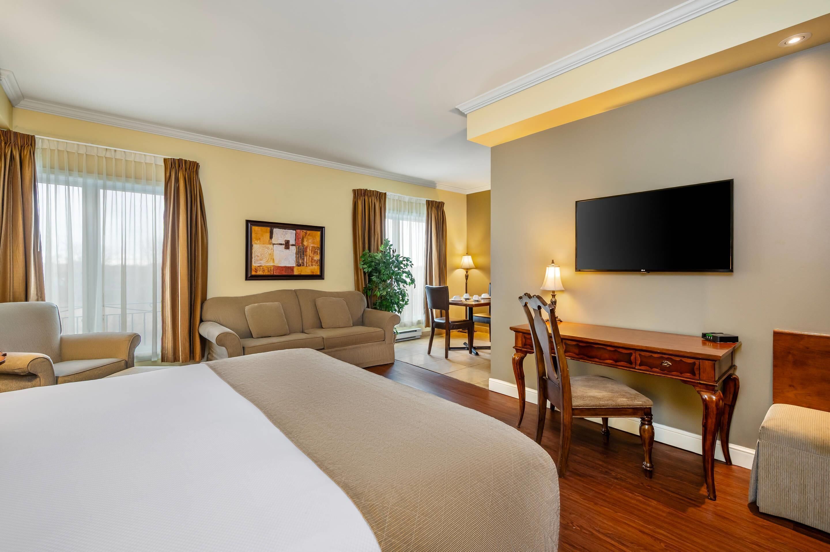 A hotel room with a large bed, a desk, a chair, a television, and a dining table.