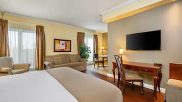 A hotel room with a large bed, a desk, a chair, a television, and a dining table.