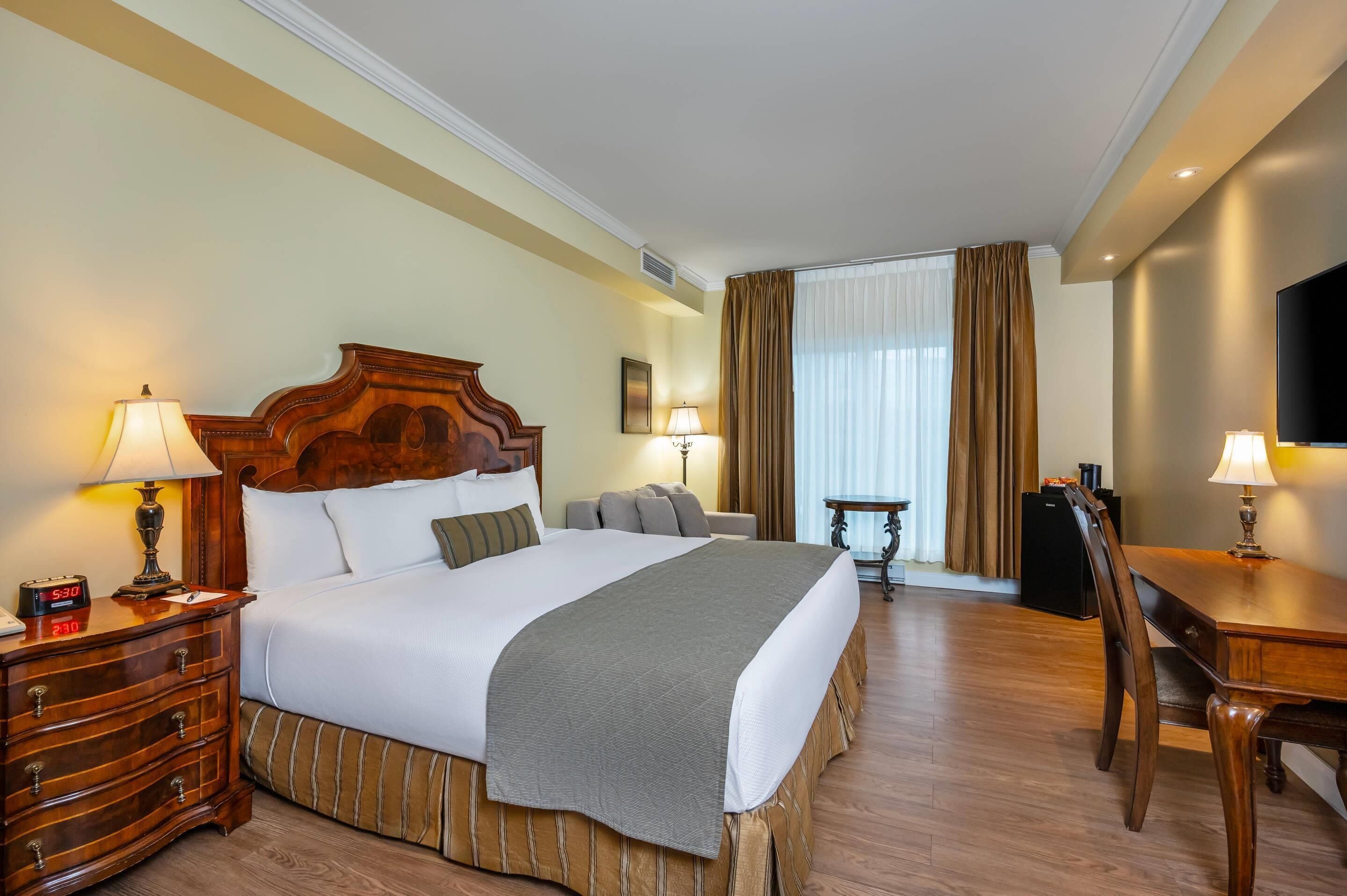 Une chambre d’hôtel avec un grand lit, des tables de chevet, un bureau, une chaise, une télévision et une fenêtre avec des rideaux.
