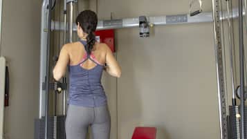 A woman using a cable machine in a gym with a red bench and dumbbells on the floor.