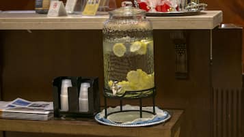 Un dispensador de bebidas con un frasco de vidrio, rodajas de limón y un plato sobre una mesa de madera.