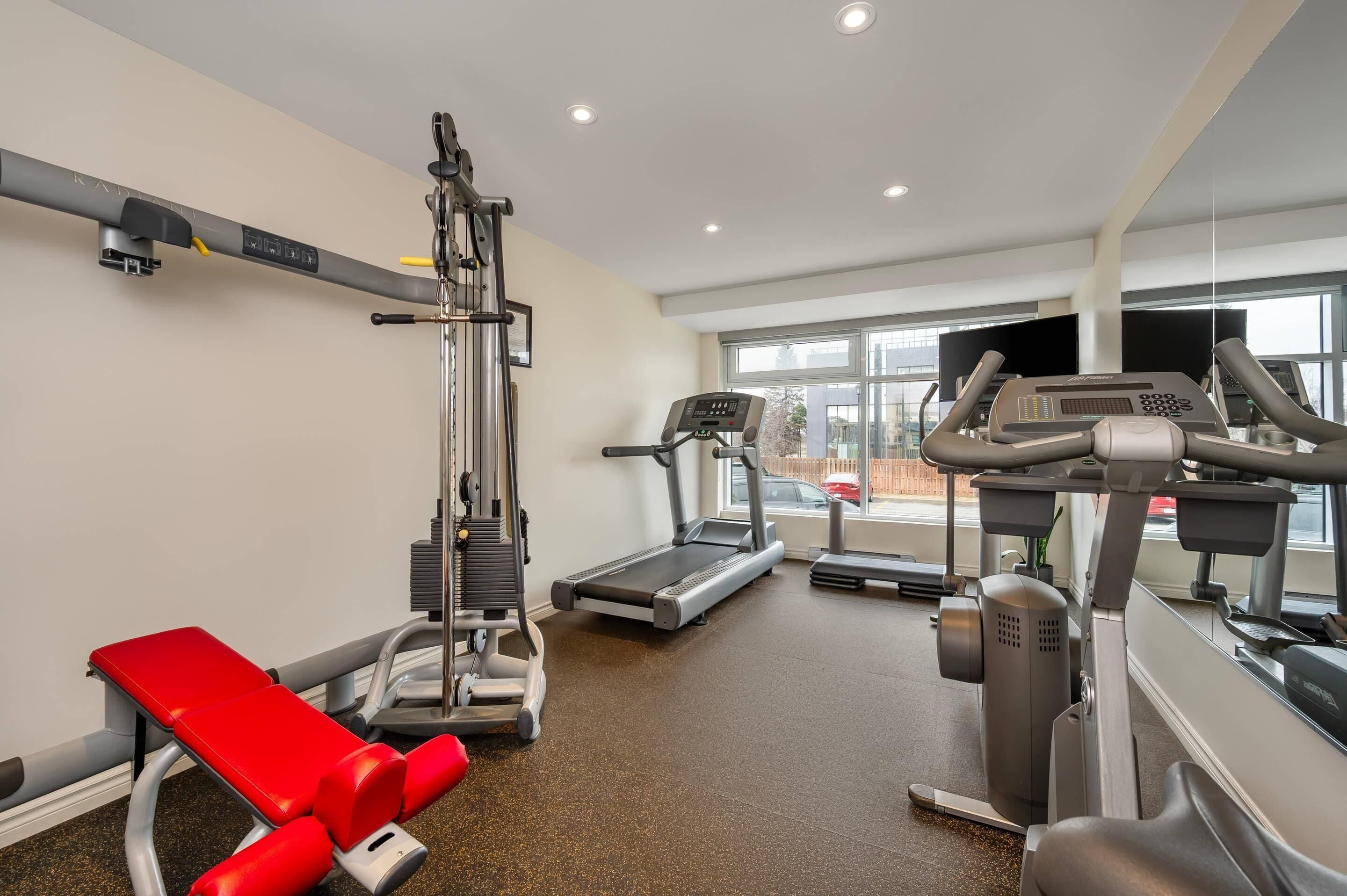 A gym with a treadmill, weight machine, and red bench.