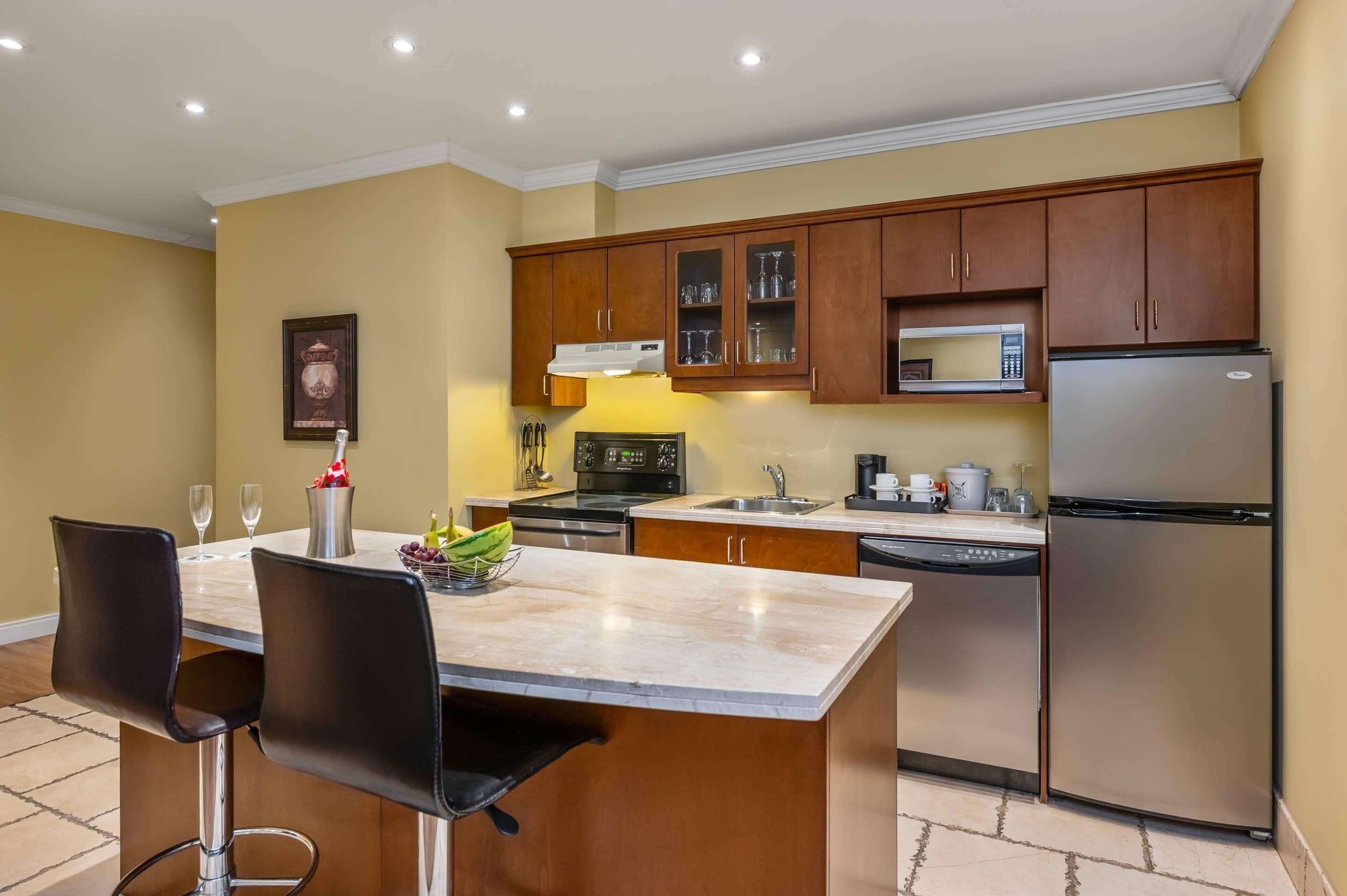 Cocina moderna con armarios de madera, un refrigerador de acero inoxidable, un microondas y una zona de comedor con dos sillas y una encimera de mármol.
