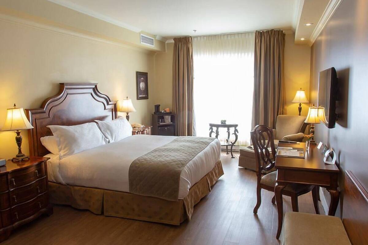 A hotel room with a large bed, two bedside tables with lamps, a desk with a chair, and a television mounted on the wall.