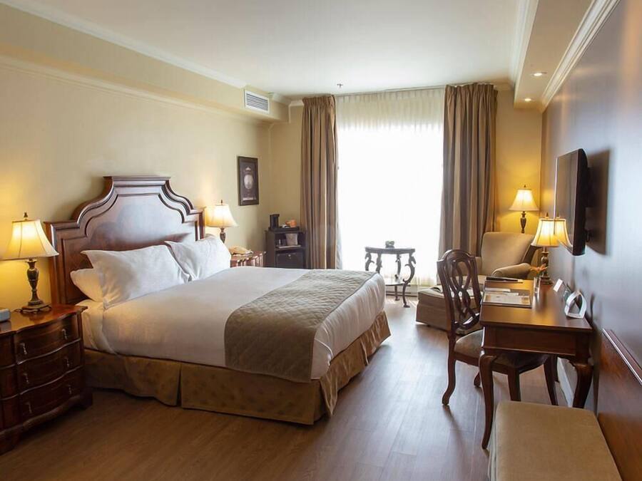 Habitación de hotel con una cama grande, dos mesitas de noche con lámparas, un escritorio con silla y un televisor en la pared.