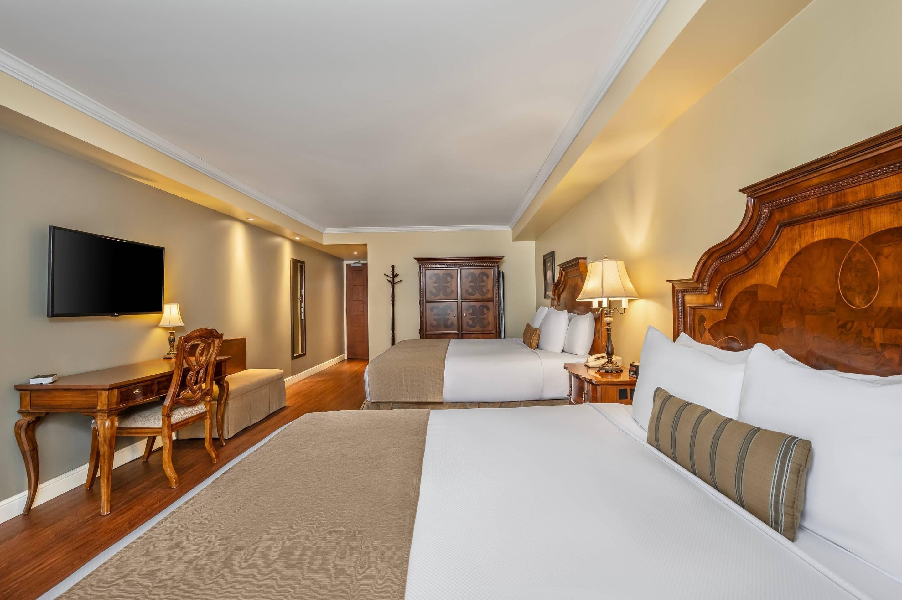 A hotel room with a large bed, a desk, a chair, a television, and a wardrobe.