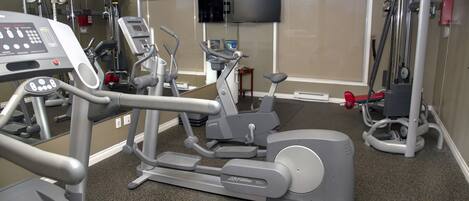A gym with various exercise equipment, a television mounted on the wall, and a mirror reflecting the equipment.