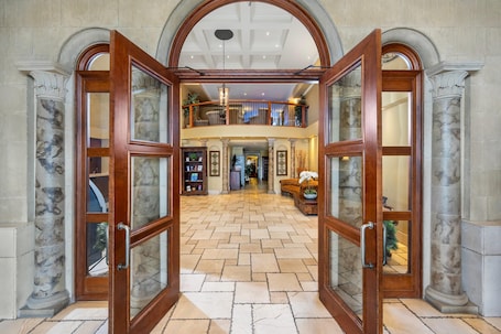 A grand foyer with a high ceiling, marble columns, and a central open space leading to a second-floor balcony.