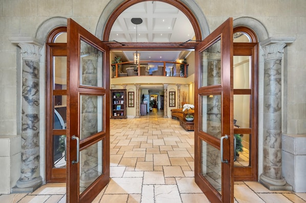 A grand foyer with a high ceiling, marble columns, and a central open space leading to a second-floor balcony.