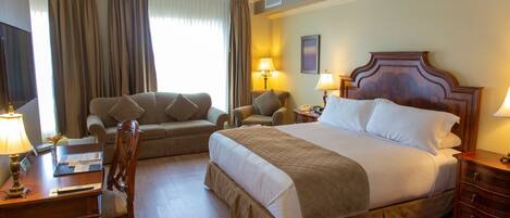 A hotel room with a bed, two armchairs, a desk, and a nightstand.