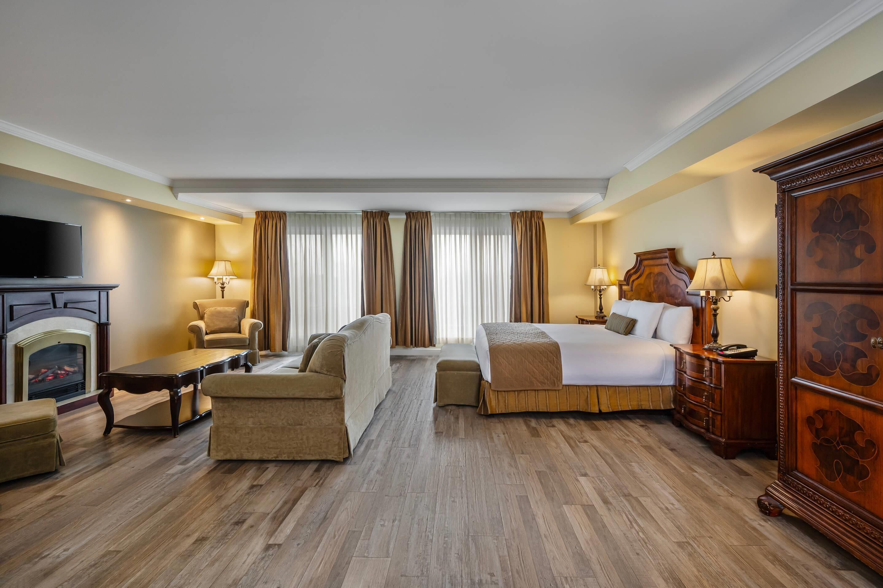 Habitación de hotel con cama, sofá, sillón, suelo de madera, chimenea y televisor.