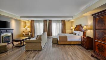 Een hotelkamer met een bed, bank, fauteuil, houten vloer, open haard en een televisie.