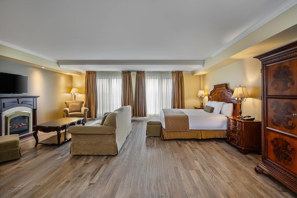 Habitación de hotel con cama, sofá, sillón, suelo de madera, chimenea y televisor.