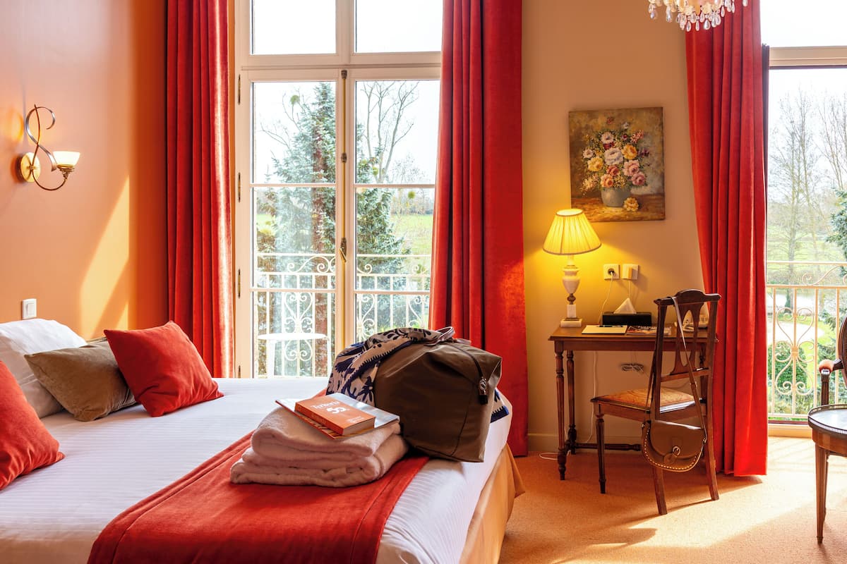 A hotel room with a bed, a desk with a lamp, a chair, and a painting on the wall.
