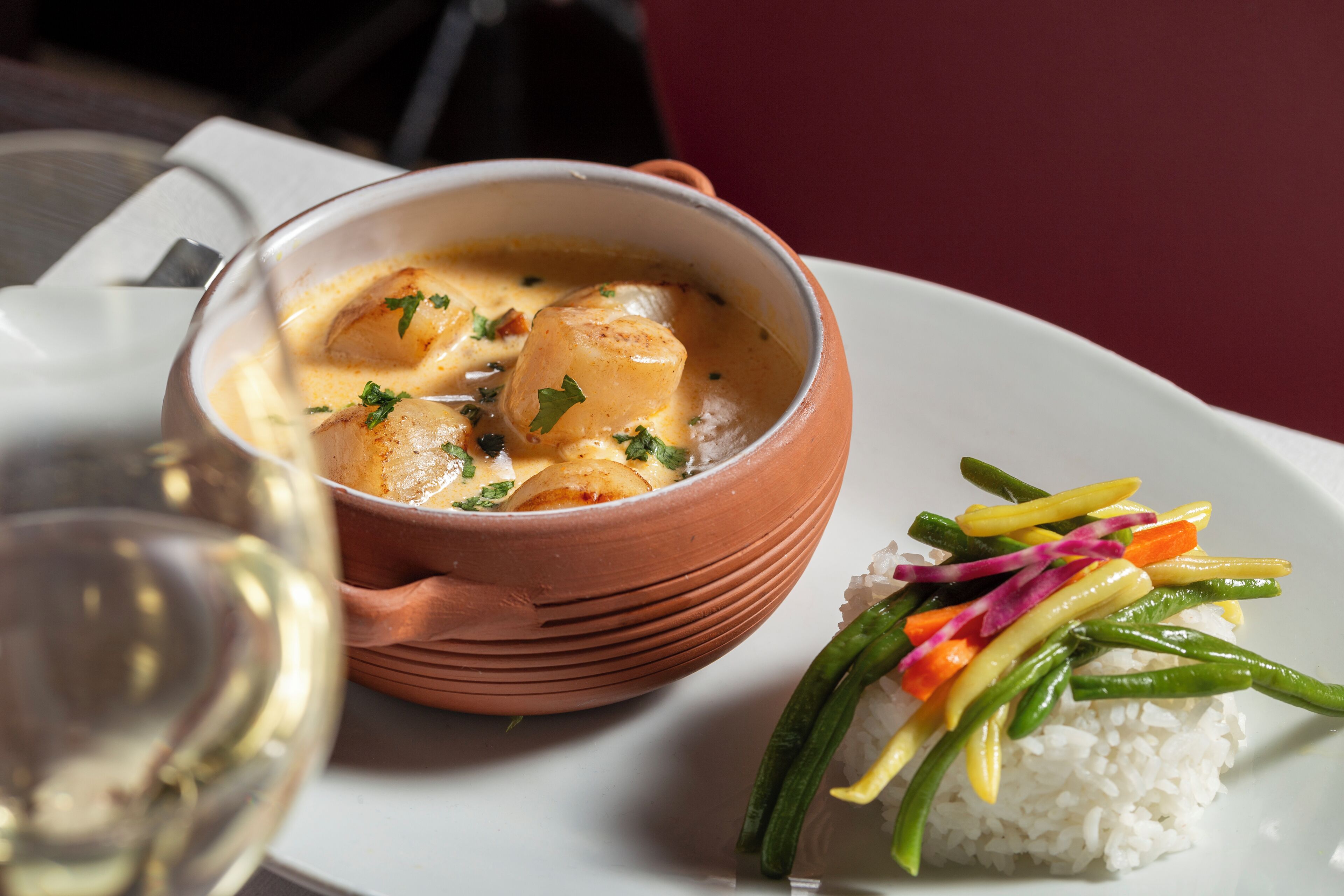 Un tazón de sopa cremosa con hierbas, un plato de arroz con verduras y una copa de vino blanco.
