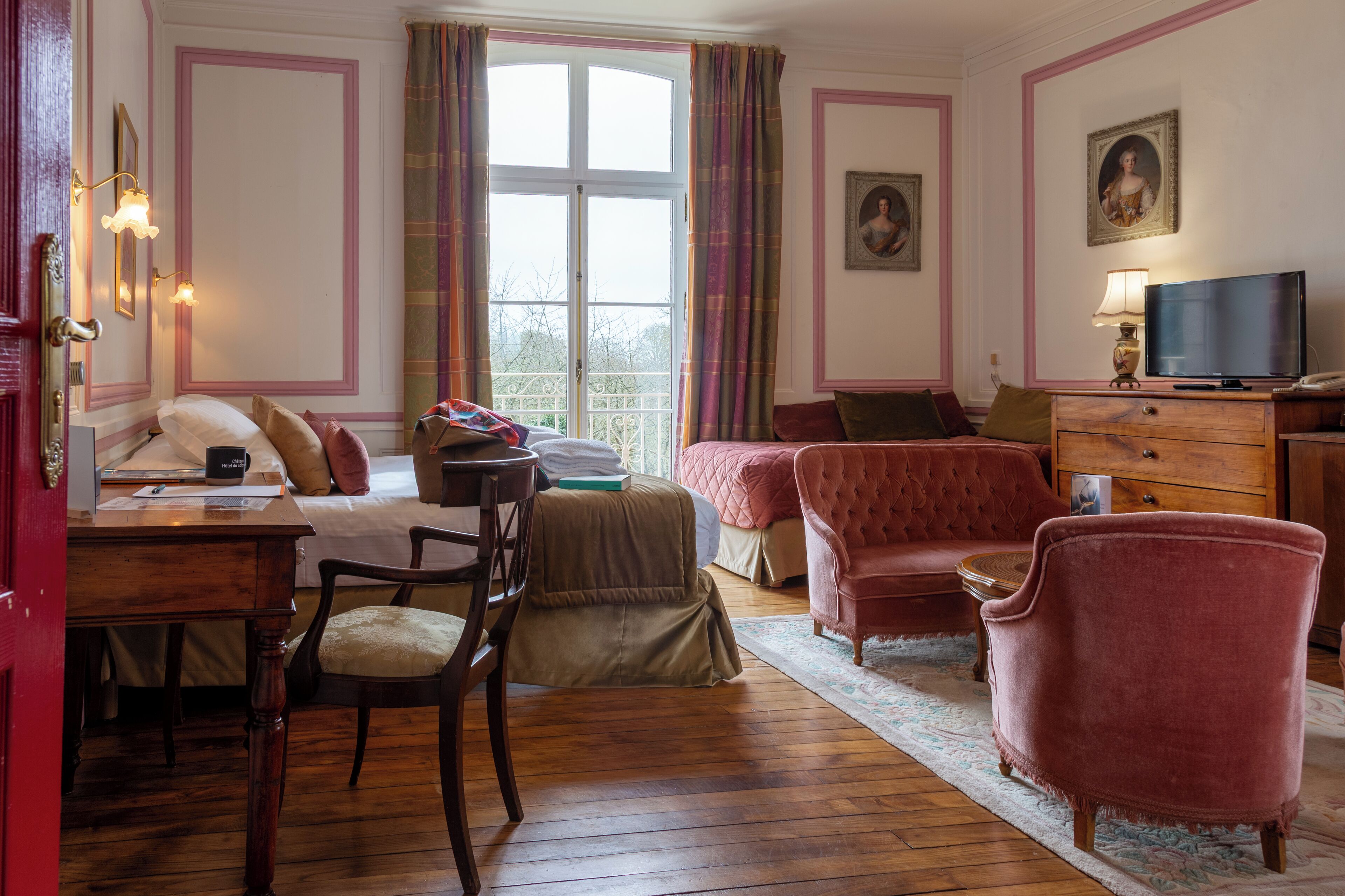 Une pièce comprenant un lit, un bureau avec une chaise, un fauteuil rouge, une télévision et une fenêtre avec des rideaux.